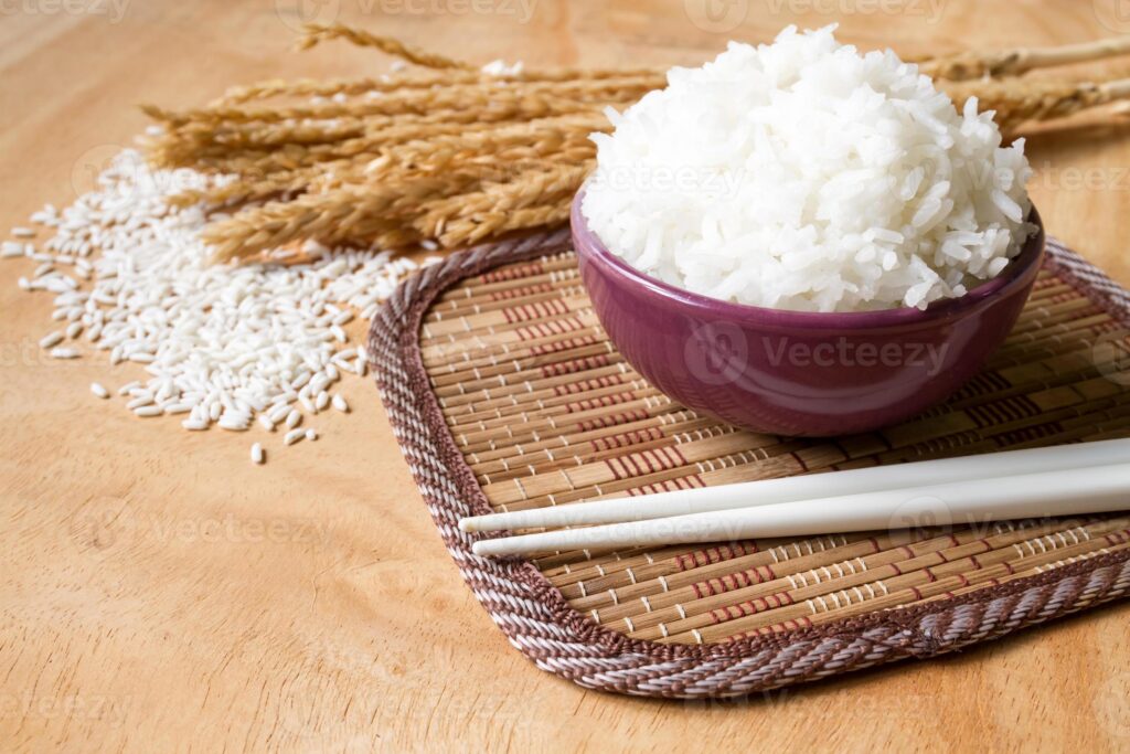 cooked rice in bowl with raw rice grain and dry rice plant on wooden table background photo